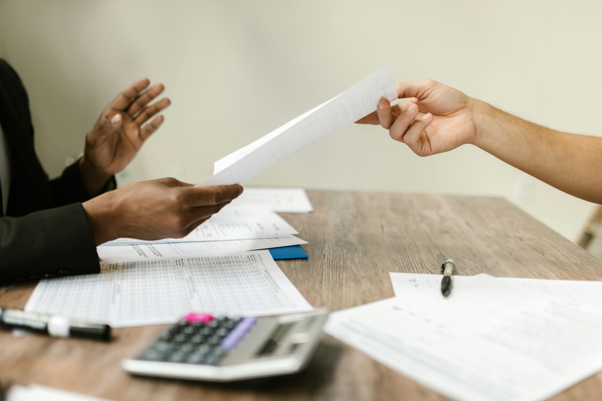 Two professionals exchanging documents in a corporate setting, emphasizing collaboration and paperwork.